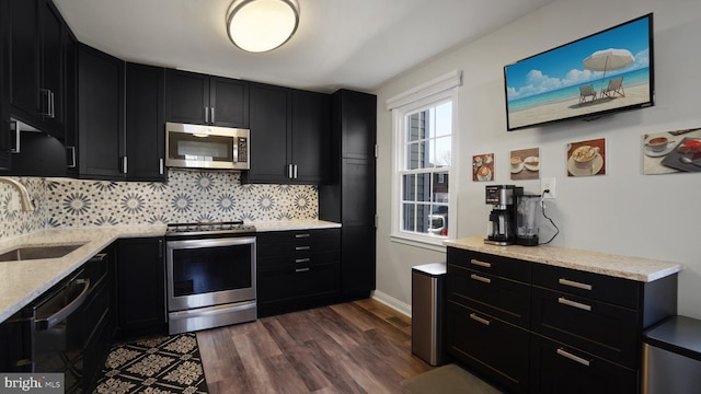 kitchen featuring a sink, appliances with stainless steel finishes, decorative backsplash, dark wood finished floors, and dark cabinets