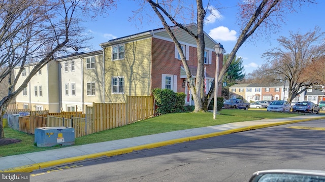 view of front of house featuring a residential view, brick siding, fence, and a front lawn