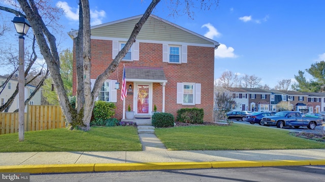 view of front of home featuring brick siding, fence, a front lawn, and a residential view