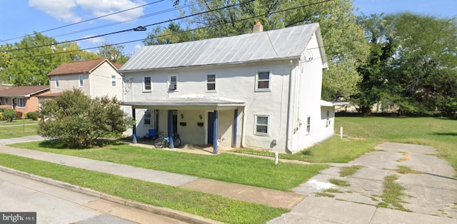 view of front of home featuring a front lawn, metal roof, a chimney, and stucco siding