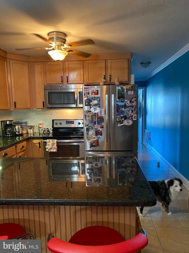 kitchen with ornamental molding, a ceiling fan, dark stone countertops, stainless steel appliances, and tile patterned flooring