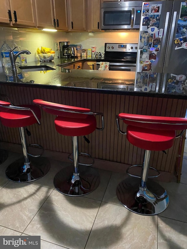 bar featuring a sink, stainless steel appliances, decorative backsplash, and tile patterned floors