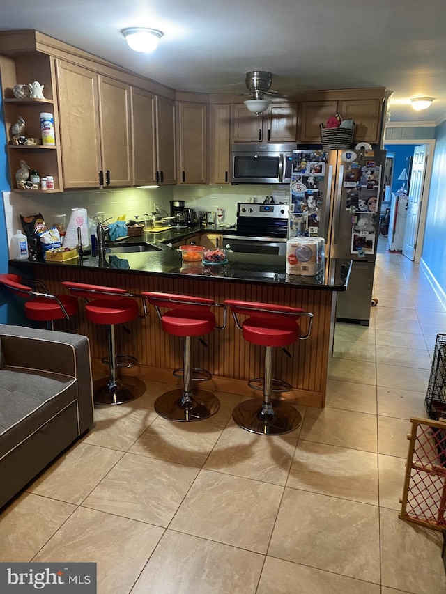 kitchen featuring a sink, dark countertops, appliances with stainless steel finishes, a peninsula, and light tile patterned floors