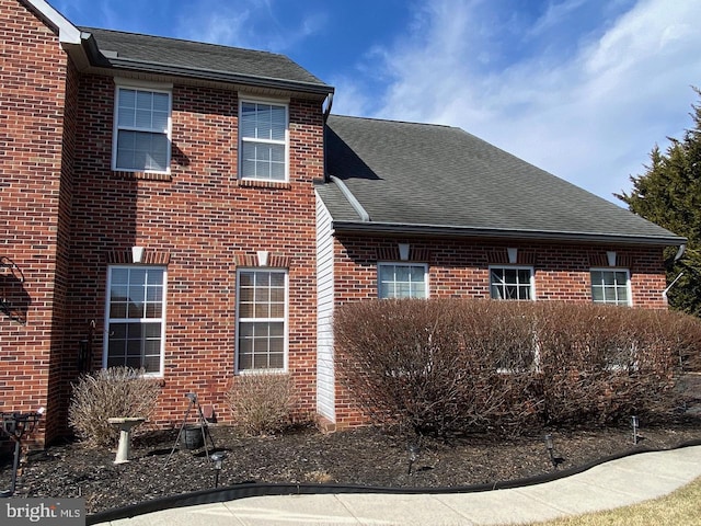 view of side of home with brick siding and roof with shingles