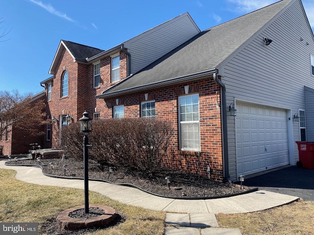 view of side of home with aphalt driveway, brick siding, roof with shingles, and an attached garage