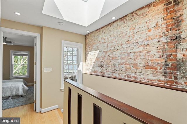 hallway featuring brick wall, baseboards, light wood-type flooring, recessed lighting, and a skylight