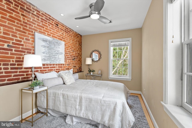 bedroom with ceiling fan, baseboards, and brick wall