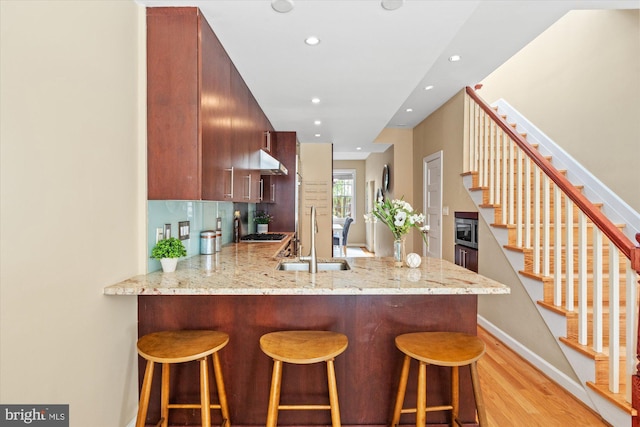 kitchen featuring stainless steel microwave, a breakfast bar, a peninsula, light wood-style floors, and a sink