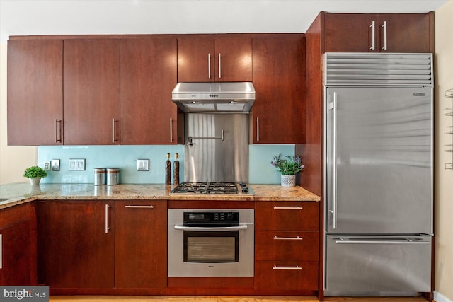 kitchen with under cabinet range hood, stainless steel appliances, and light stone countertops