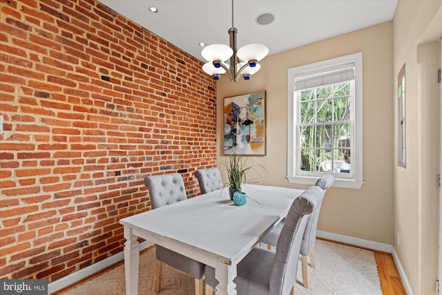 dining room with a notable chandelier, light wood-style floors, brick wall, baseboards, and an accent wall