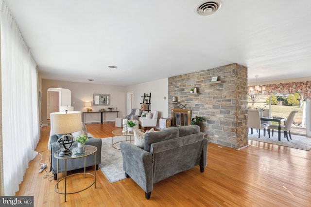 living area with wood finished floors, visible vents, an inviting chandelier, a fireplace, and arched walkways