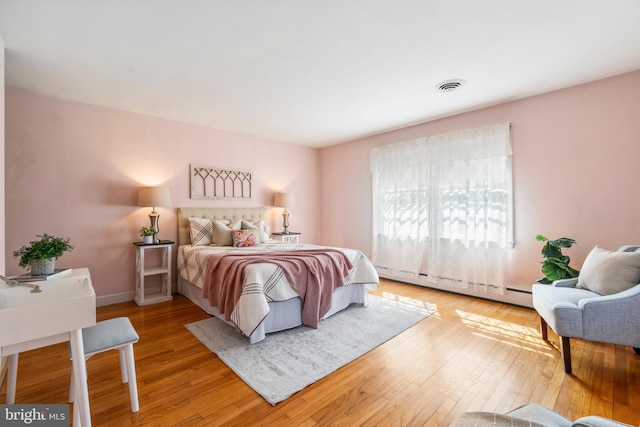 bedroom featuring hardwood / wood-style floors, baseboards, visible vents, and a baseboard radiator