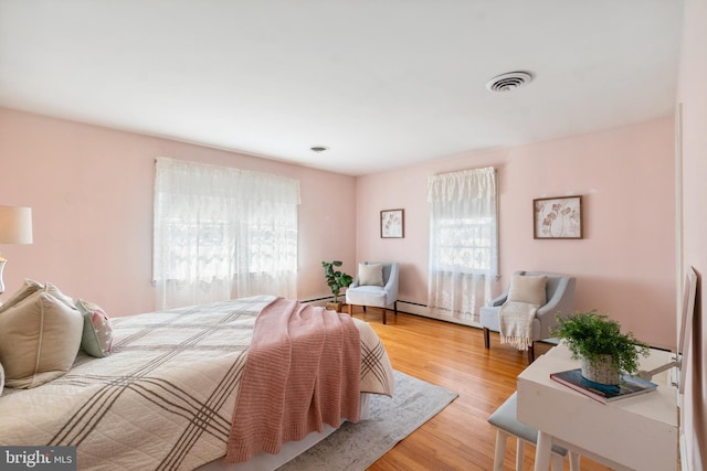 bedroom featuring visible vents, multiple windows, wood finished floors, and a baseboard radiator