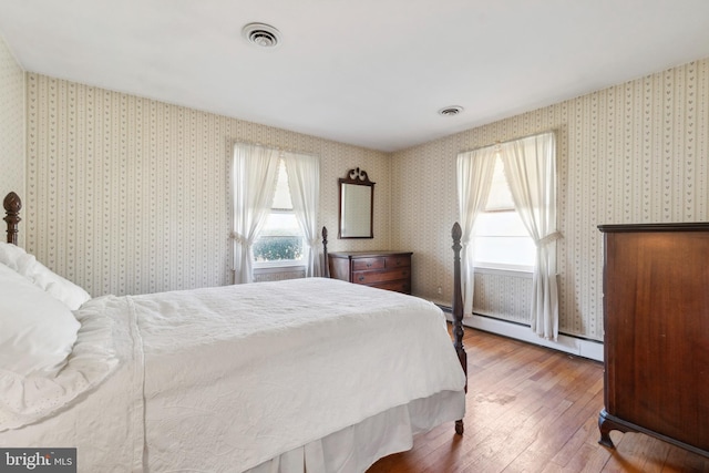 bedroom with multiple windows, a baseboard radiator, wallpapered walls, and wood-type flooring