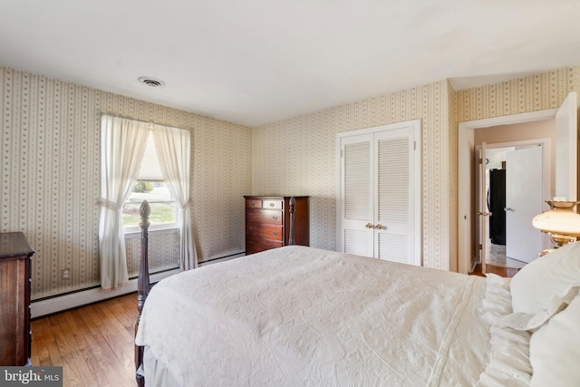 bedroom featuring a baseboard heating unit, wood-type flooring, a closet, and wallpapered walls