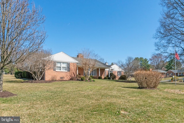 view of front facade with crawl space, brick siding, a front yard, and a chimney