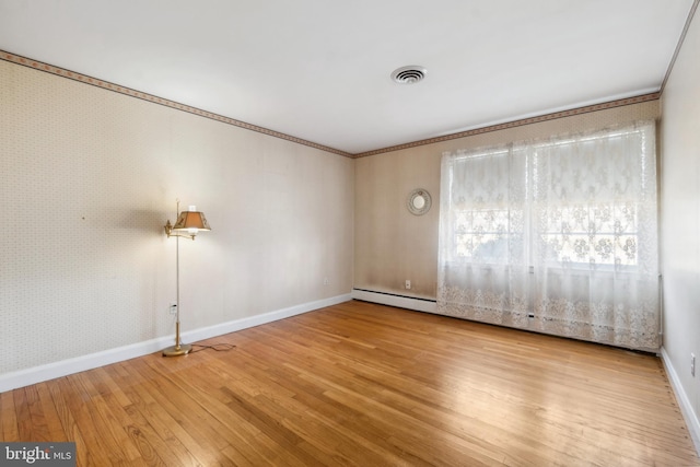 spare room featuring visible vents, ornamental molding, wood finished floors, wallpapered walls, and baseboards