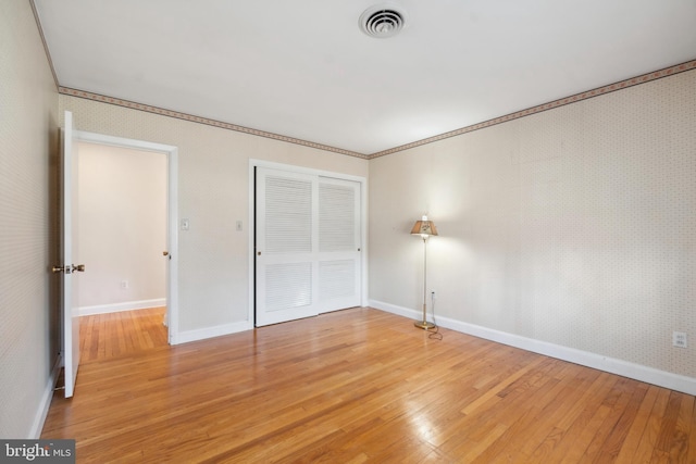 unfurnished bedroom with visible vents, light wood-style flooring, a closet, wallpapered walls, and baseboards