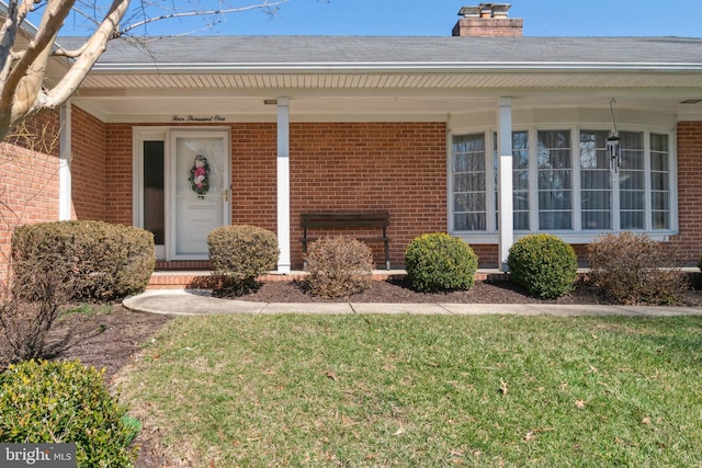 doorway to property featuring a yard, brick siding, a porch, and a chimney