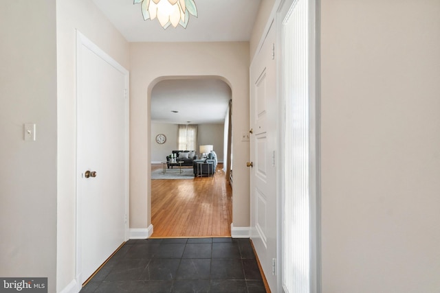 hallway featuring dark tile patterned flooring, baseboards, and arched walkways