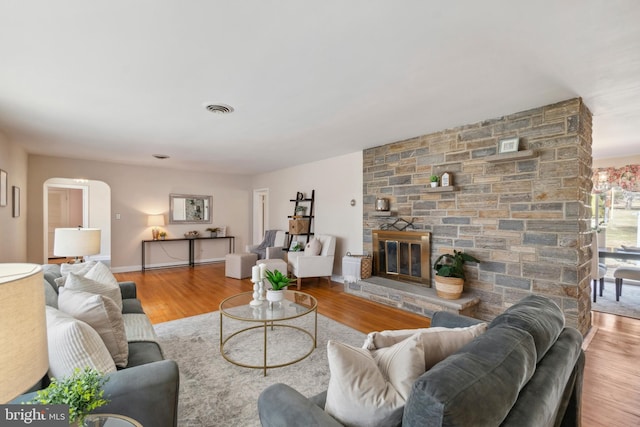 living room featuring arched walkways, a stone fireplace, visible vents, and wood finished floors