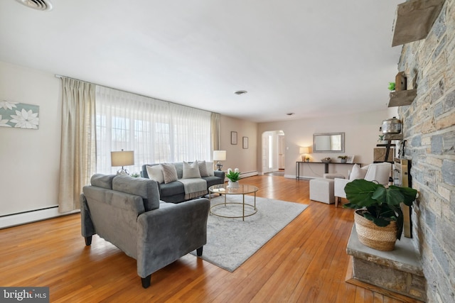 living room featuring a stone fireplace, light wood-style floors, and baseboard heating