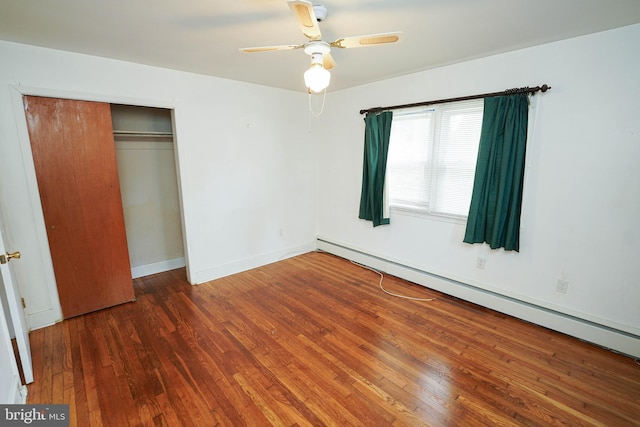 unfurnished bedroom featuring a baseboard heating unit, baseboards, wood finished floors, a closet, and a ceiling fan