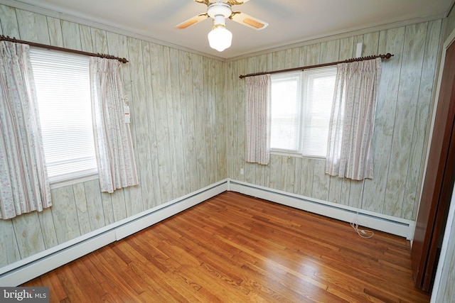 unfurnished room featuring baseboard heating, wood finished floors, and a ceiling fan