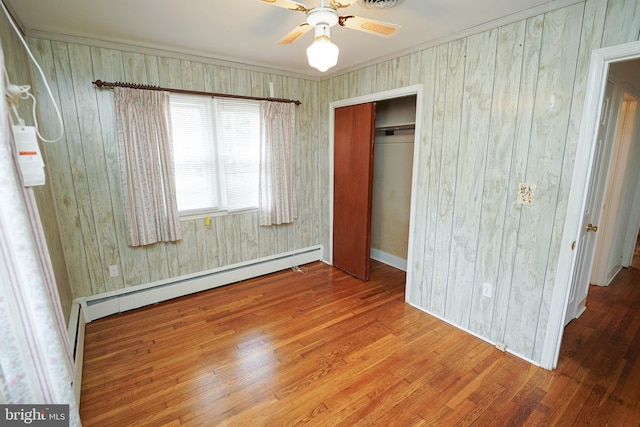 unfurnished bedroom with ceiling fan, a baseboard heating unit, a closet, and wood finished floors