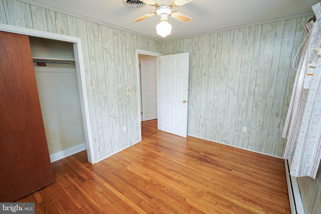 unfurnished bedroom featuring visible vents, a baseboard heating unit, a closet, wood-type flooring, and ceiling fan