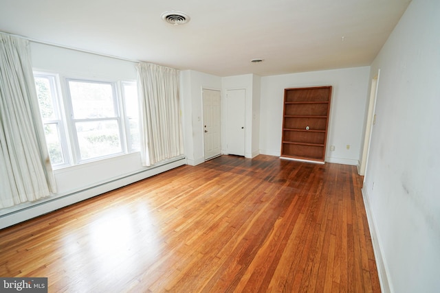 spare room with visible vents, built in shelves, a baseboard heating unit, wood finished floors, and baseboards