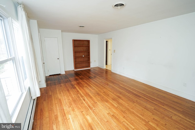 empty room with visible vents, baseboard heating, baseboards, and hardwood / wood-style flooring