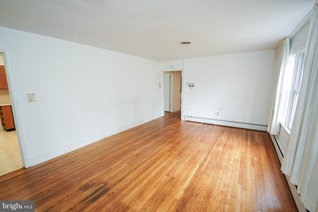 spare room with visible vents, a baseboard heating unit, light wood finished floors, baseboards, and baseboard heating