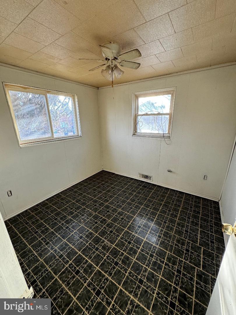 unfurnished room featuring visible vents, plenty of natural light, ceiling fan, and dark floors