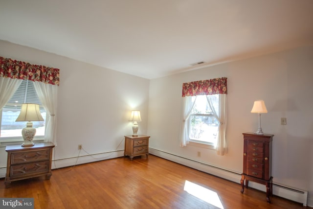 bedroom with a baseboard heating unit, visible vents, and wood finished floors