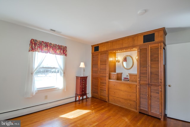 unfurnished bedroom featuring a baseboard radiator, visible vents, and wood finished floors