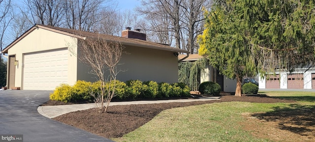 view of home's exterior featuring a detached garage, stucco siding, a chimney, a yard, and an outbuilding