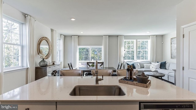 kitchen with a kitchen island with sink, a sink, open floor plan, light stone countertops, and dishwasher