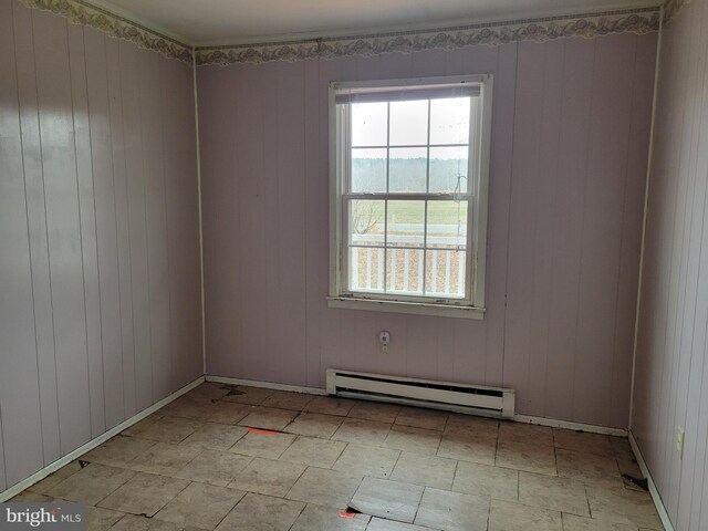 unfurnished room with a baseboard heating unit, baseboards, and wood walls