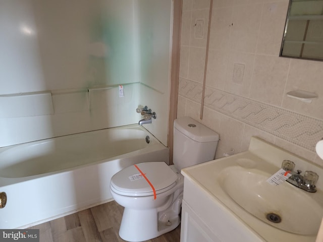 full bath featuring toilet, wood finished floors, tile walls,  shower combination, and vanity