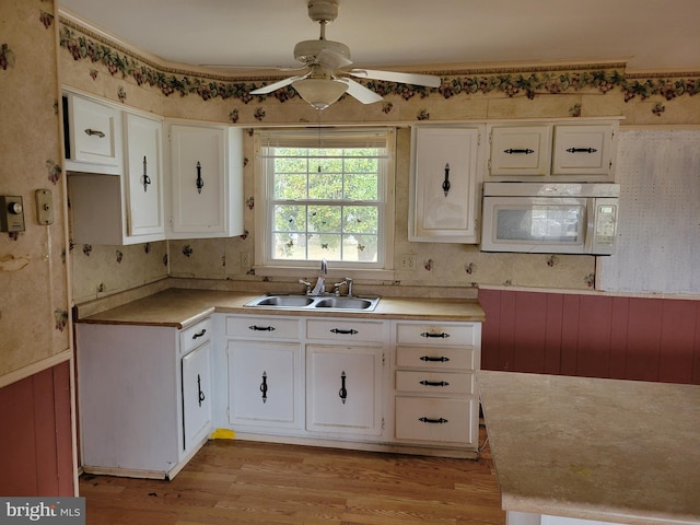 kitchen featuring light wood-type flooring, a ceiling fan, a sink, white cabinets, and white microwave