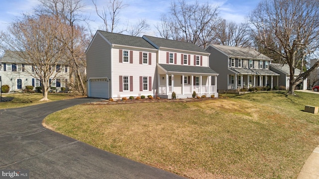 colonial home featuring a front lawn, aphalt driveway, a residential view, covered porch, and a garage