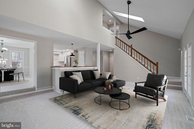 carpeted living area featuring visible vents, baseboards, stairs, a skylight, and high vaulted ceiling