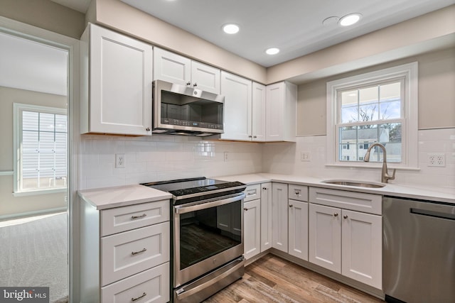 kitchen featuring a healthy amount of sunlight, light countertops, appliances with stainless steel finishes, white cabinetry, and a sink