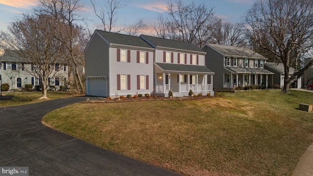 colonial inspired home featuring aphalt driveway, a lawn, a porch, and a garage