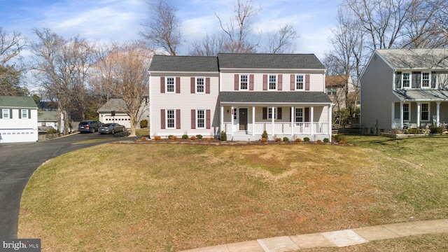 colonial home featuring a front yard, covered porch, and roof with shingles