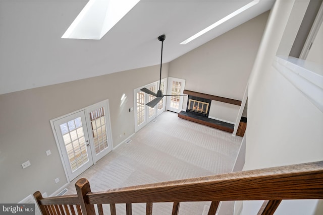 staircase featuring high vaulted ceiling, a skylight, french doors, a glass covered fireplace, and carpet flooring