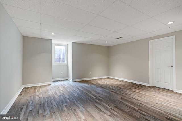 empty room featuring a drop ceiling, baseboards, and wood finished floors