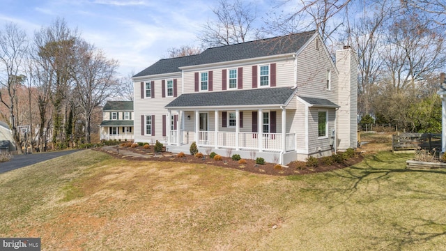 view of front of home with covered porch, a chimney, a front lawn, and roof with shingles