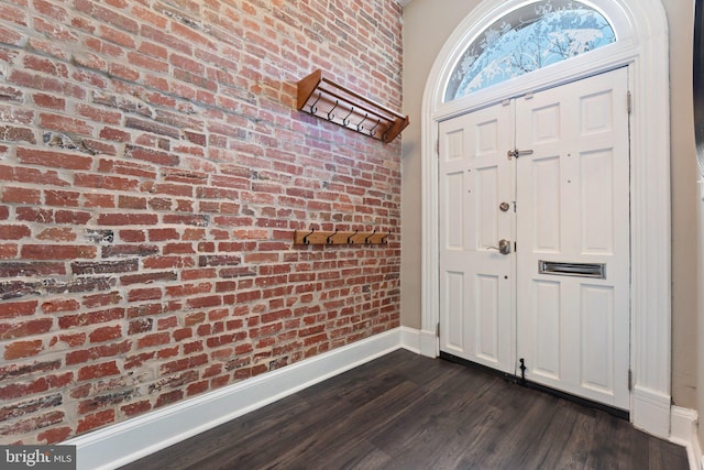 entrance foyer with brick wall, dark wood-type flooring, and baseboards